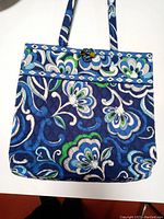 Front view of the tote handbag showing blue Mediterranean floral pattern with fabric handles and button loop closure.