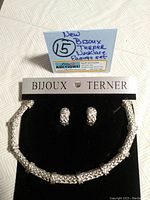 Front view of necklace and earrings mounted on black card branded Bijoux Terner with handwritten auction lot tag.