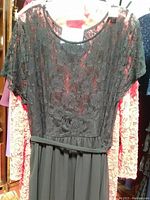 Dress displayed on mannequin showing black lace floral top with sheer short sleeves and solid black skirt bottom with fabric tie belt.