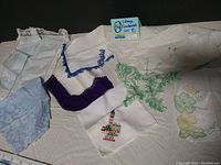 Seven vintage cotton handkerchiefs of various colors and embroidered or printed designs laid flat showing lace and crochet trims and a Big Ben London motif.