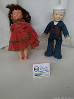 Photo showing both dolls side by side: Toddy girl doll in red crochet dress and Sailor Boy doll in blue uniform with white hat.
