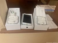 Apple iPhone SE in box with wired EarPods, wall charger adapter, and multiple boxes of IQIYI branded Lightning cables around it.