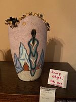 Front view of Bill Standefer vase showing turquoise figure, terracotta pot designs, pink-speckled ceramic base, and 22k gold rim inlay.