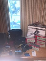Lot overview showing cameras, bags, slide magazines, and scanner box on wooden surface near window with curtain background