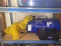 Photo of the blue Campbell Hausfeld 7 gallon air tank with attached yellow coiled air hose and black compressor sitting on a shelf.
