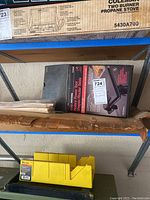 Cardboard shelving with boxed rotary power tool shaper router table and wood strips below a Coleman propane stove box