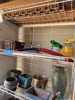 Photo showing multiple flower pots on a metal rack including ceramic and metal varieties, with some visible handheld tools and spray containers above.