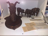 Photo showing mounted antelope head plaque in front with elephants and paperwork behind on shelf