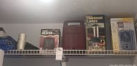 Top shelf view showing ceramic electric heater in box, brown Coleman cooler, fluorescent lantern - Greatland brand, and small ultra electric heater in box.