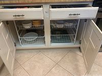 Kitchen cabinet lower drawers and doors open showing various sizes and types of bowls including Corningware and Pyrex glass bowls stored in wire rack drawers.