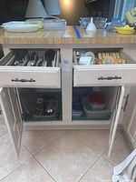 Kitchen cabinet with drawers open showing assorted kitchen utensils, plastic storage containers, and bowls.