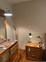 Standing wooden floor lamp with silver adjustable shade next to two black desk lamps on wooden nightstand with jewelry spread out