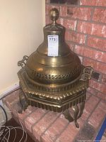 Assembled brazier with lid and finial on tripod base, front-left view on brick hearth