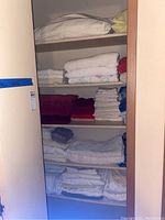 Shelves with multiple folded linens including a white pillow, yellow pillowcase, towels in red, white, blue, and cream, and floral patterned floor mats or bed linens.
