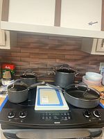 Four pieces of KitchenAid cookware on stove with cutting boards stacked to the side