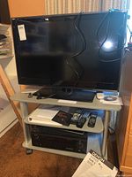 LG 32-inch flat screen TV on gray rolling stand with cords and remotes on shelves