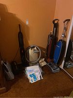 Overview of three upright vacuums, central vacuum canister, hose and loose attachments/manuals
