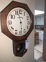 Full side view showing frontal octagonal clock face with brown wood finish and pendulum compartment below.