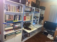 Four large white laminate wall shelves filled with books, with two middle fold-down shelves partially lowered, and storage compartments at the bottom with cabinet doors and silver-tone handles.