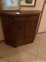 Front view of wooden hall cabinet showing two paneled doors with decorative metal hardware and beveled top edge.