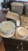 Metal and glass bakeware pans on kitchen counter including loaf pans, casserole dish with lid, and ramekins