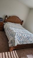 Picture of queen size wooden bed frame with bedding, showing side and headboard.