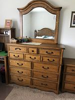 Front view of the wooden dresser with multiple drawers and the attached mirror reflecting a bed headboard.