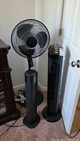 Photo showing three fans: one pedestal fan with adjustable height and two black tower fans of different sizes.