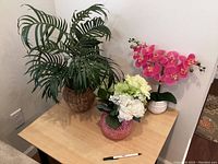 Three artificial decorative plants displayed on a wooden table against cream walls.