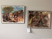 Two framed village scene prints shown side by side, depicting rural life with a camel and figures.
