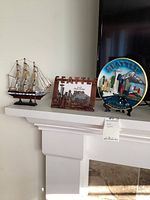 Three items displayed on a white mantel: sailing ship model, Seattle copper colored picture frame, and Seattle collectible plate