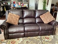 Front view of dark brown leather reclining sofa with rolled arms and two patterned throw pillows