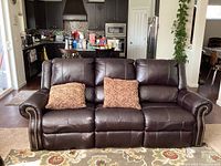 Front view of the three-seat brown leather sofa in living area with two throw pillows on seat