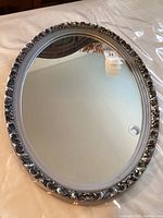 Full view of the oval mirror showing the decorative silver-tone frame and glass mirror surface