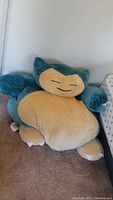 Full front view of the Snorlax bean bag showing the plush blue and beige design with its smiling face and small claws visible.