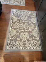 Rectangular throw rug with beige and cream floral pattern on wooden floor by dark furniture.