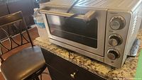 Photo showing the front of Oster toaster oven with three control knobs, glass door, and handle on granite countertop