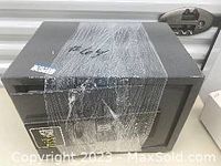 Black metal safe wrapped in plastic, featuring digital keypad and key lock mechanism on front.