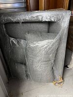Blue grey fabric sofa wrapped in protective plastic, viewed from the back showing cushioning and fabric texture
