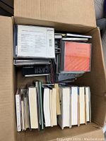 Box with assorted music CDs stacked on top of mixed books