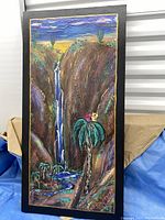 Front view of the canvas painting depicting a desert canyon with a waterfall, palm trees, and cacti. The painting has a textured style with rich colors and a black frame border.
