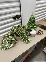 Photo showing ceramic Christmas tree, holly wreath, and small decorations on table