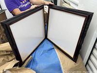 Two dark wooden diploma frames with glass fronts and white mats sized for 11x14 diplomas placed on a blue surface.