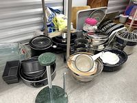 Photo shows various kitchen items including pots, pans, baking dishes, strainers, cutting boards and small kitchen appliances grouped on the floor.