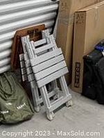 Three folding tables stacked upright against a wall, two are painted grey and one is painted brown.