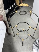 Black iron plate stand with three circular tiers and tripod legs, rope accents on joints and handle