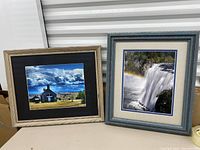 Two framed artworks side by side: a colorful building painting and a waterfall print.