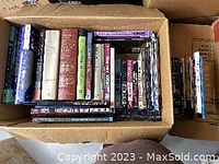 Photo shows two cardboard boxes filled with various hardcover and paperback books in different sizes and colors.
