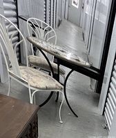 Side view of white iron chairs with fabric cushions next to black iron table stand and cement tabletop decorated with dragonflies.