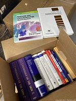 Photo of 12 medical textbooks in cardboard box focusing on pathology and dermatology.